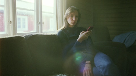 Kvinne som sitter i sofaen og bruker mobilen.