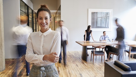 Ung kvinne smiler på et kontor med andre ansatte