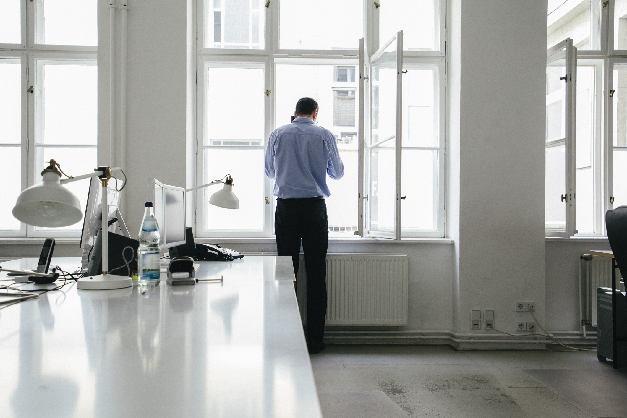 Forretningsmann snakker på mobilen og står ved vinduet på et tomt kontor