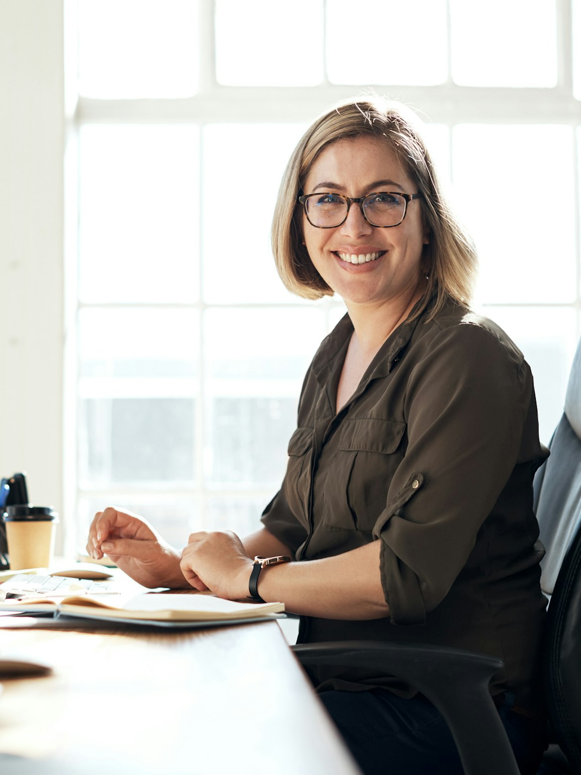 A woman is sitting by a desk, smiling at the camera.