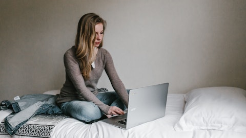 En dame sitter i sengen og jobber på en laptop