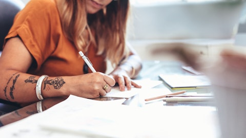 En kvinne med tatoveringer sitter og skriver på et ark.