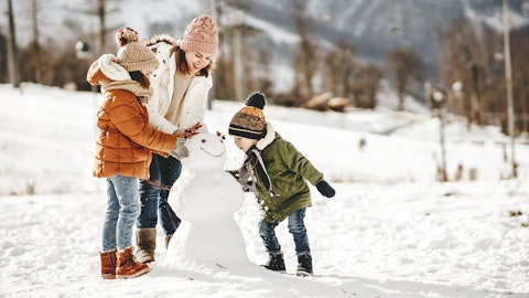 En dame bygger snømann med to barn. Foto