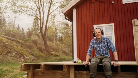 Smilende mann bygger terrasse rundt et rødt hus