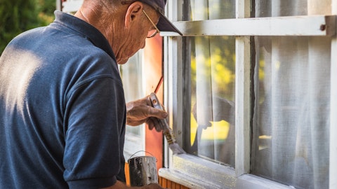En eldre mann maler vinduskarmene på huset sitt.