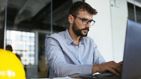 En konsentrert mann med skjegg og briller jobber på laptopen sin.