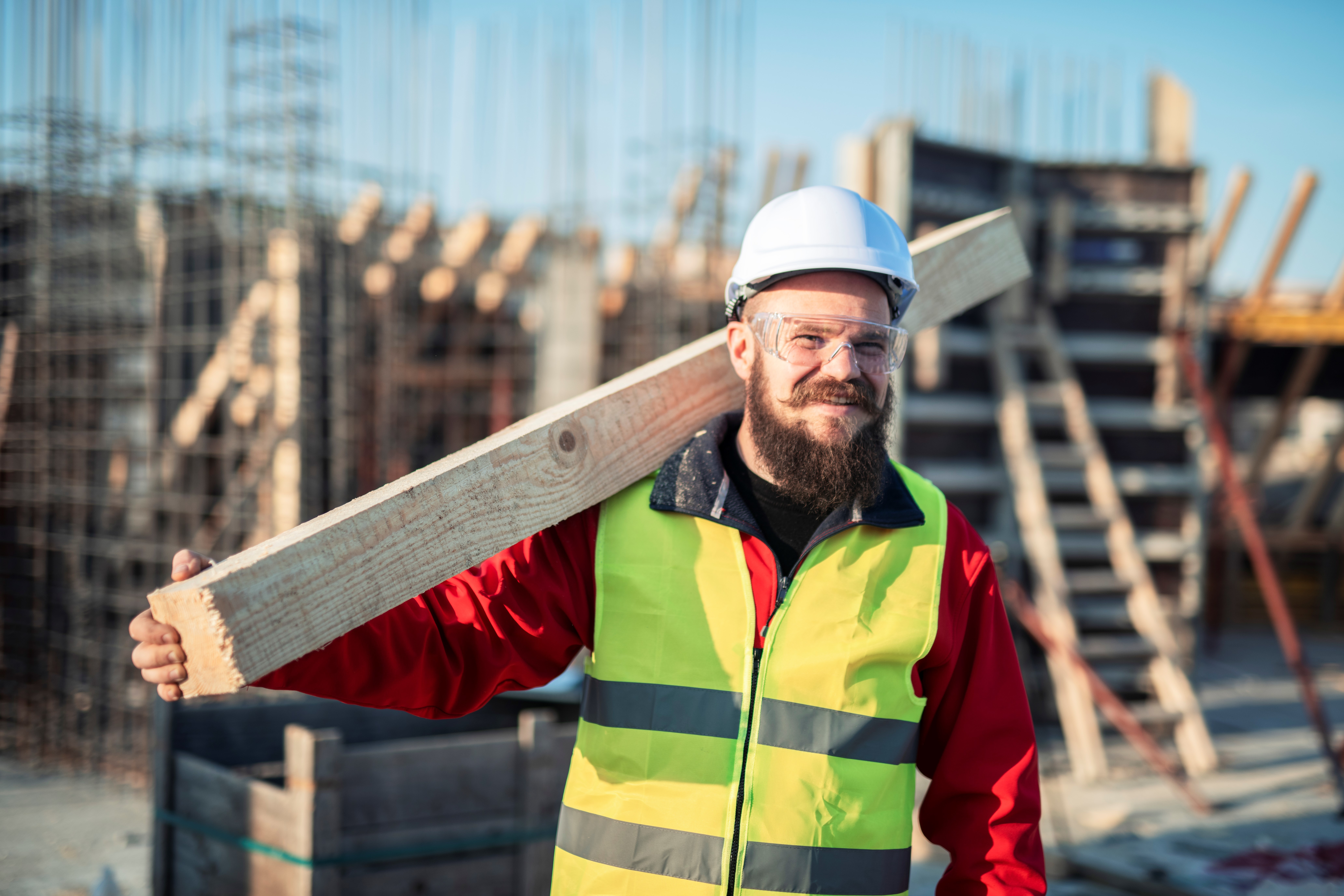 Byggearbeider bærer noe og smiler mot kameraet.