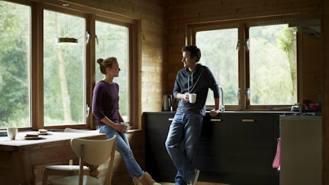 Et par står på stua i en hytte og holder en samtale med en kopp kaffe i hånden.