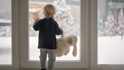 En liten gutt står og ser ut av verandadøren mens han holder en kosebamse.