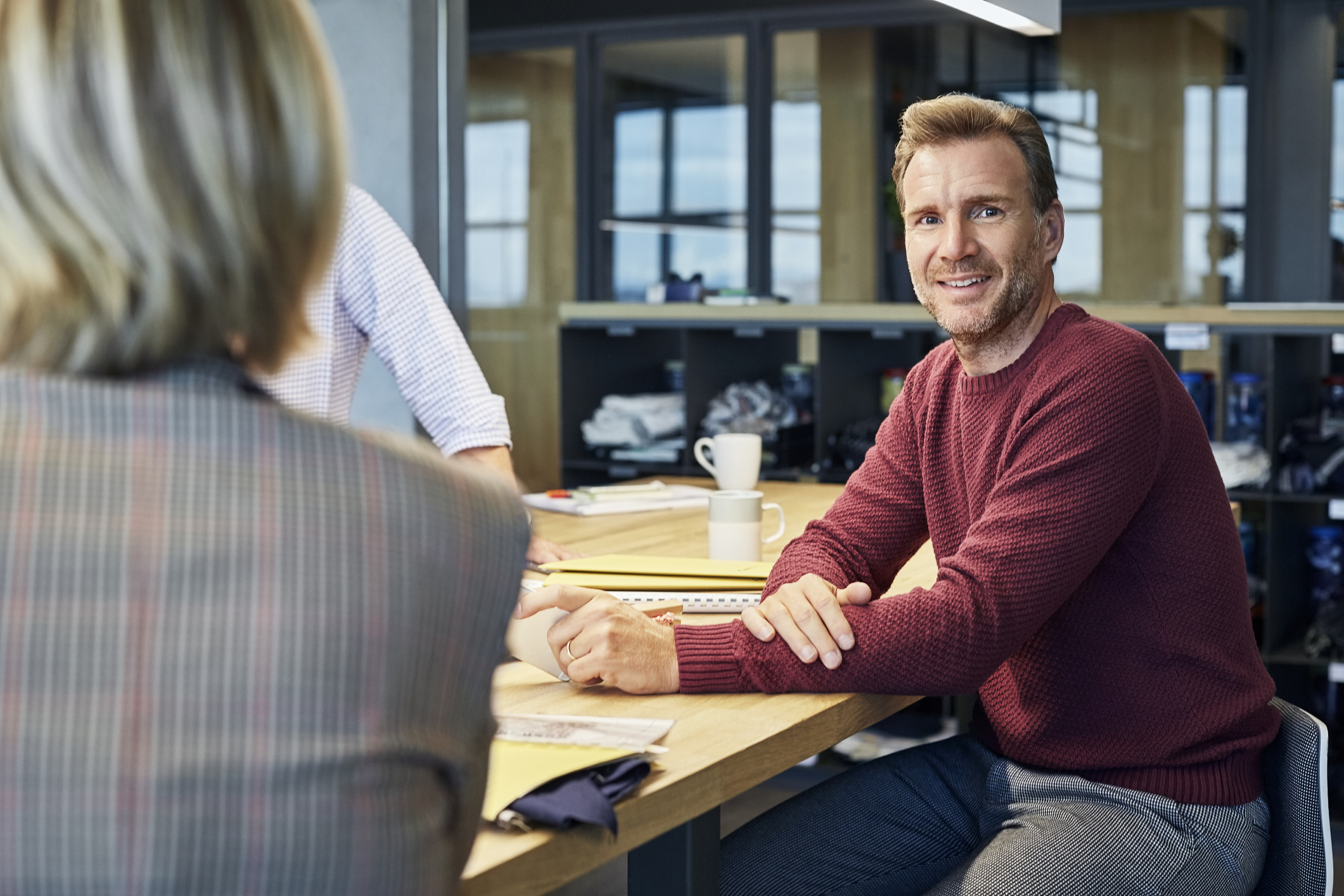 En mann sitter ved et bord og ser på kameraet.