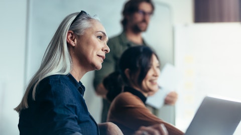 En smilende kvinne under et møte med flere deltakere.