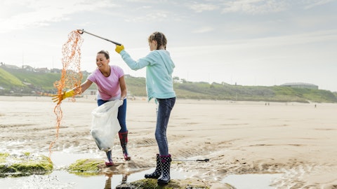 To kvinner fisker plast fra vannet ved stranden