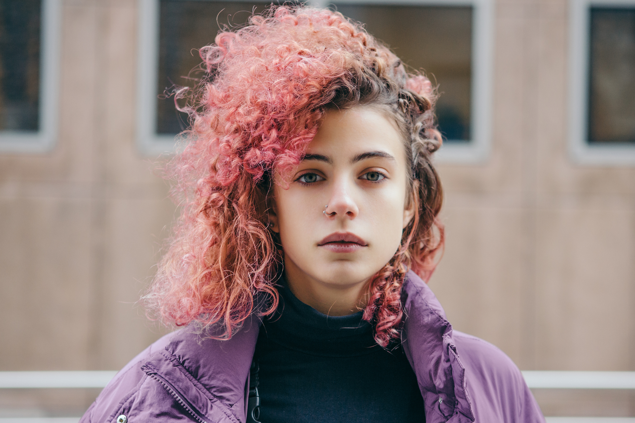 En ung kvinne med rødt hår og nesering ser alvorlig mot kameraet.