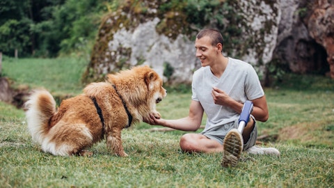En mann med benprotese sitter på gresset sammen med hunden sin.