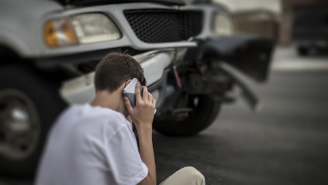 Gutt som snakker i telefon foran en bil som har kræsjet.