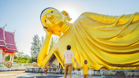 En mann holder sønnen sin i hånden foran en stor Buddha.