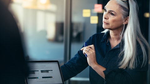 En dame ditter ved en laptop og holder en penn. Foto