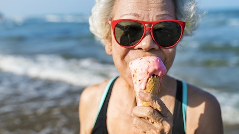 En eldre dame spiser iskrem på stranden.