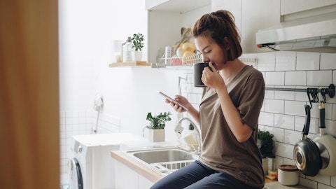 Kvinne som leser på mobilen mens hun sitter på kjøkkenbenken.