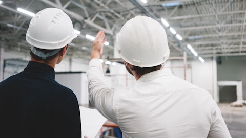 To menn med hjelmer ser utover et lagerområde og peker. Foto