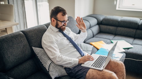 En mann med skjorte og slips sitter i en sofa i underbuksen og vinker til en laptop