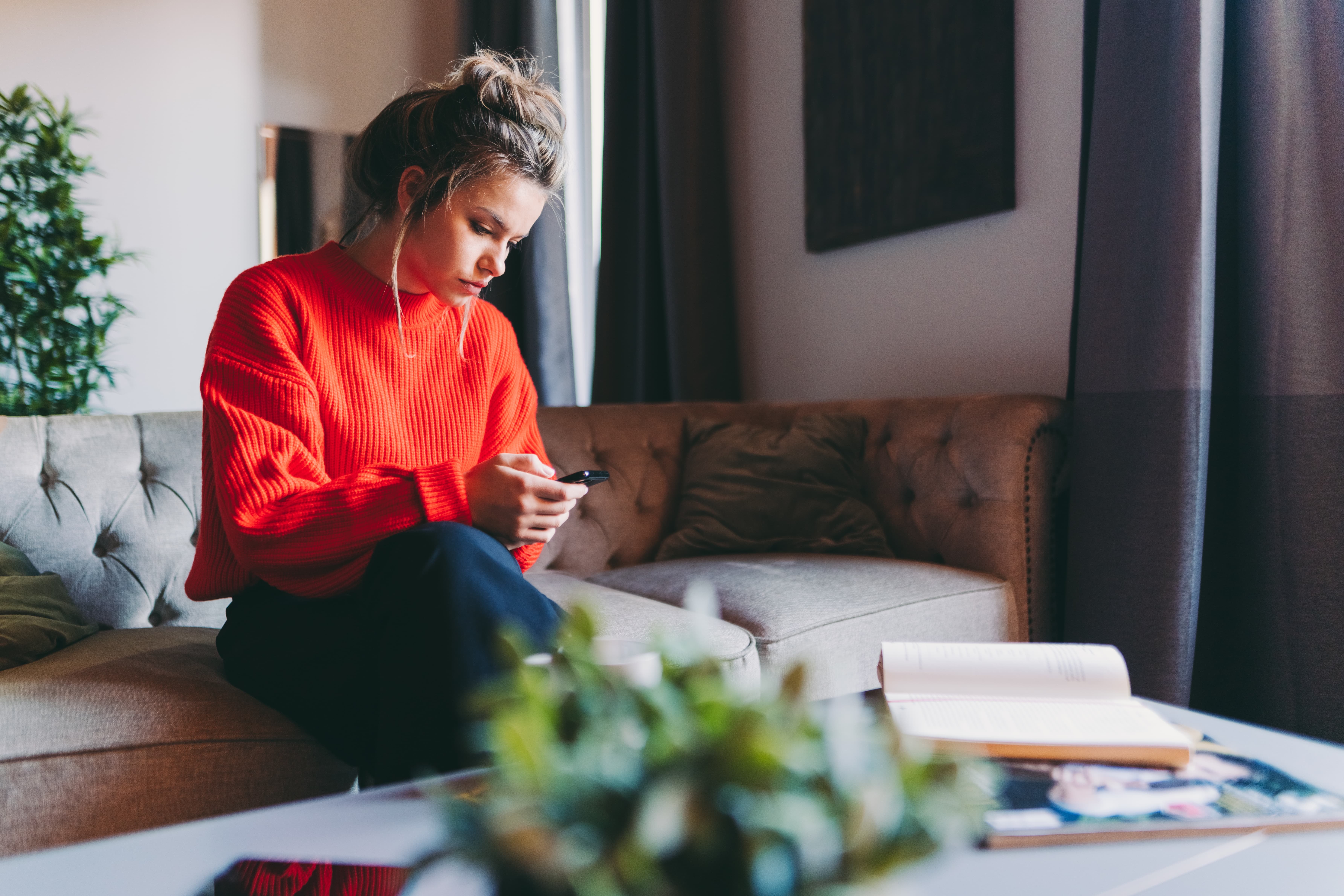 En dame sitter i en sofa og ser på telefonen sin. Foto