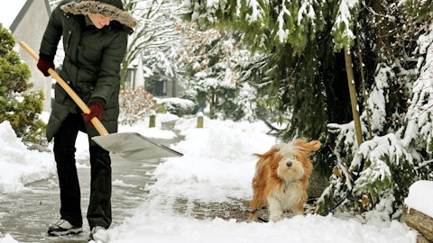 Mann som måker utenfor huset med hunden sin.