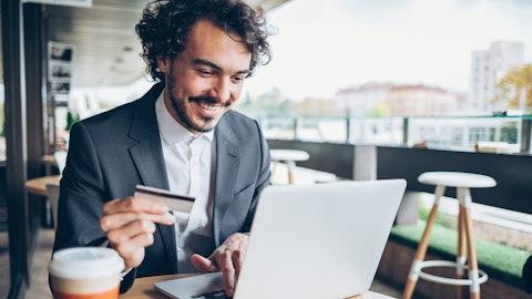 En mann  i dress skriver på en laptop mens han holder opp sitt kredittkort