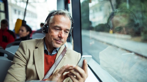 Mann sitter på bussen med hodetelefoner og sjekker noe på telefonen.