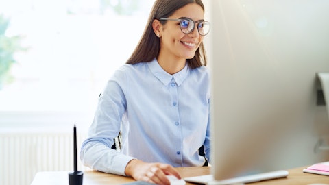 Glad kvinne i lyseblå skjorte arbeider foran en PC-skjerm.