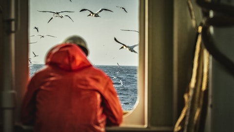 mann i rød regnfrakk ser ut over havet fra vinduet av et skip